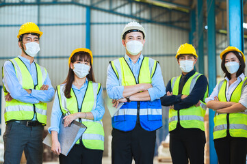 The factory employee consists of engineers, foreman, technicians, and related department staff. Wear a mask, hard hat, and vest. Stand to pose in line looking focus at the camera. Teamwork concept.