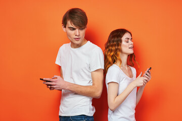 cheerful young couple in white t-shirts phones entertainment technology orange background