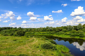 Sesupe River, Kaliningrad Region. Cumulus clouds are reflected in the river water. Green meadows in summer