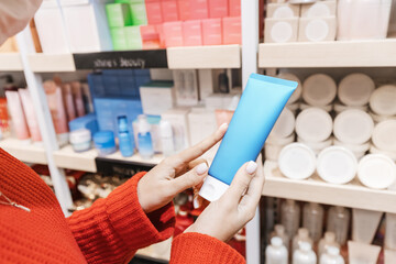 Woman customer chooses and buys cosmetics in a store or pharmacy and holds a tube of moisturizing...