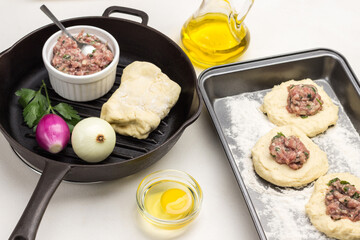 Stuffing of meat on pieces of raw dough on baking pan.