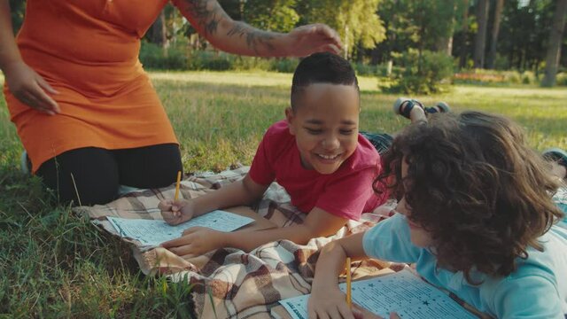 Close-up of handsome mixed race boy peeping into exam sheet of classmate while young teacher catching schoolboy on cheating outdoors. Cheerful multiethnic diverse pupils writing examination test.