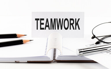 Text TEAMWORK on paper card,pen, pencils, glasses,financial documentation on table - business concept