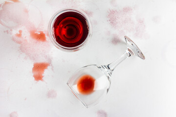 glass of red wine and overturned glass with leftover wine on a white background, drenched and...