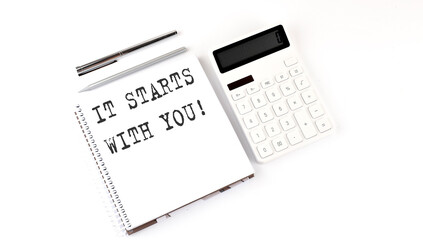 Notepad with text It starts with You with calculator and pen. White background. Business