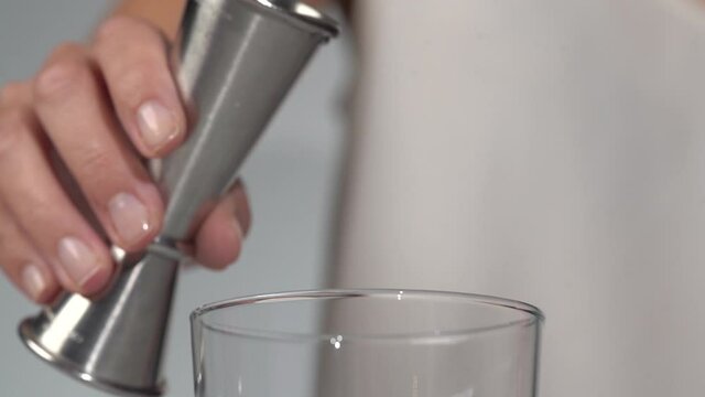 Woman bartender pouring transparent alcoholic liquid from metal jigger into clear class close up slow motion - Powered by Adobe