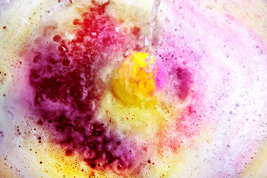 Dissolving color bath bomb in water, closeup.