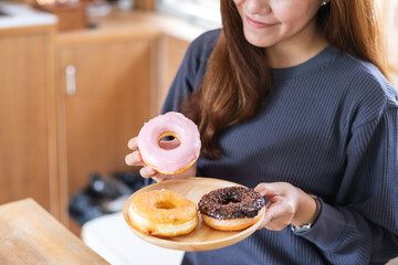 Closeup image of a beautiful young asian woman holding and eating donut at home