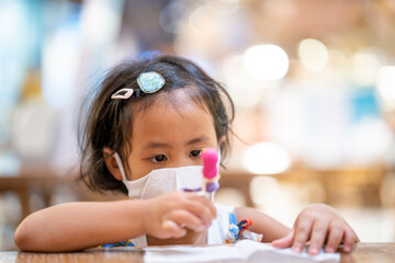 Cute small girl wearing protective face mask sitting at wooden table in shopping mall.