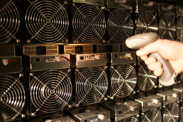 Controller in uniform scans ASIC bitcoin miners with barcode scanner in warehouse. Warehouseman working in storage room. Worker scans barcodes of power supply units in service repair center.