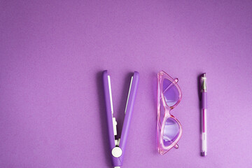 purple flat lay: hair care tool, pen, sunglasses on a purple background 