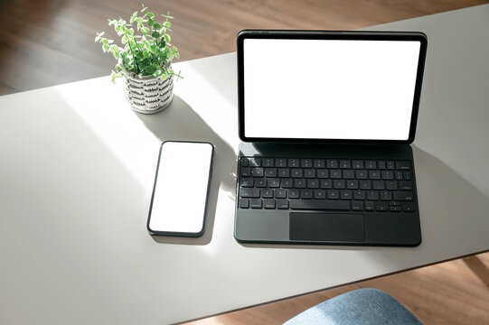 Mockup blank screen tablet with keyboard and mobile phone on white top table with morning sunlight.