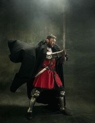 One brutal bearded man, medeival warrior or knight with dirty wounded face holding sword. Full...