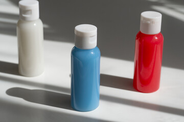 travel cosmetics in small bottles: shower gel, shampoo and conditioner. cosmetics in red, blue and white colours on a white background with shadows 