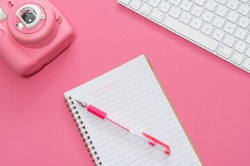 Business concept. Workspace with business accessories: keyboard, pen, notebook and fast print camera on a pink background.