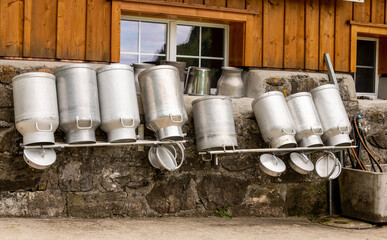 große Milchkannen vor einer Berghütte zum Trocknen auf Gestänge kopfüber gestellt.