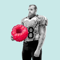 Sportive young man with huge berry on light background. Male american football player with...
