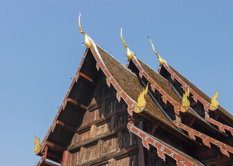 Beautiful tiered roof with golden naga decoration at ancient teak wood buddhist temple Wat Phan...