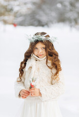 Fototapeta na wymiar Cute little girl in a wreath of fir holds fir twigs and dried flowers outdoors on a beautiful winter sunny day