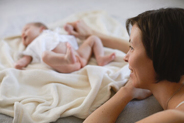 Mom and newborn girl on the bed. Caucasian mom enjoying with her infant baby on the bed in room.