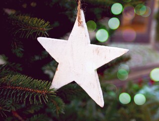 a white wooden toy in the shape of a star on a green fir-tree on the street. Christmas, New year decorations