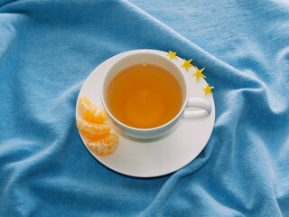 cup of tea on a blue sweater with mandarin slices on a white saucer