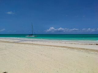 Fototapeta na wymiar Cayo Guillermo, Cuba, 16 may 2021: Nice view of Pilar beach with white sand and azure ocean against the blue sky. The catamaran with tourists stopped near the shore for swimming and snorkeling.