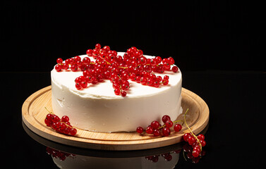 White mousse cake on black backdrop and currant decoration
