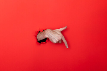 Male caucasian hand through a hole pointing against a red background