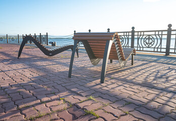 Fototapeta na wymiar Wooden benches for relaxation of an unusual shape for relaxing on the embankment, against the backdrop of the setting sun and blue sky