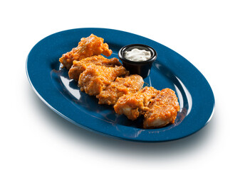 Alitas de pollo rebozadas con salsa de yogur en fuente azul sobre fondo blanco. Breaded chicken wings with yogurt sauce in blue dish on white background.
