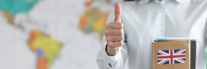 Woman holding english textbooks on background of world map and showing thumb up closeup