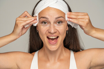 young happy woman with headband cleans her face with wet wipes