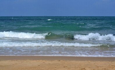 Fototapeta na wymiar View from the sandy shore to the sea, waves and white sea foam