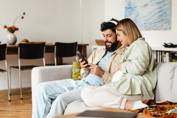 White couple using cellphone and headphones while sitting on couch