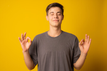 Young handsome man wearing casual t-shirt standing over isolated yellow background relax and smiling with eyes closed doing meditation gesture with fingers. Yoga concept.