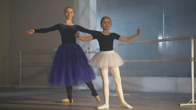 Motivated girl and confident woman doing tendu movement in ballet studio indoors. Wide shot portrait of Caucasian ballerinas rehearsing ballroom dancing in slow motion. Choreography art