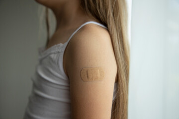 Little girl with long brown hair in white tank top got her vaccine, little's girl arm with plaster with drawn heart after vaccine