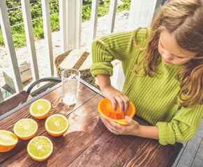 the girl child makes freshly squeezed orange juice on a manual juicer