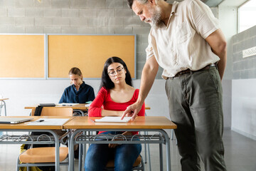 Mature caucasian man teacher helps teen girl high school student solve doubts about lesson. Copy...