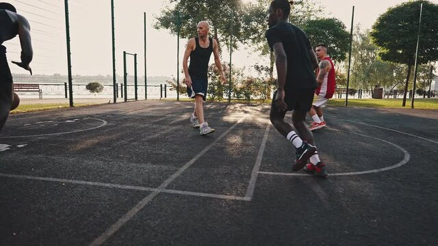 Backyard basketball team has training on the city basketball court. Young multiracial men playing basketball. Players give a high handshake to each other, throw and assist