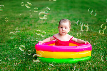 a child swims in an inflatable pool in summer on the green grass with soap bubbles, space for text