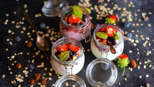 Yogurt oat muesli and fresh berries in jars rotate on a dark background. Healthy breakfast with yoghurt and fruits.
