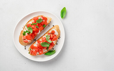 Two sandwiches with tomato, cheese, basil on a fried baguette on a gray background.