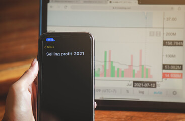 hand hold phone for making note about selling profit of trading in 2021 of his investment