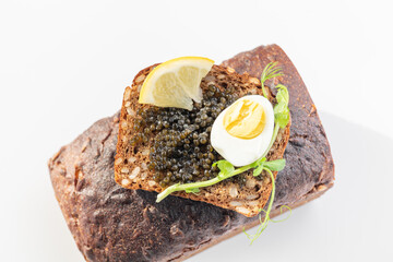Black caviar on a sandwich with eggs, lemon, greenery