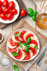 A portion of caprese salad in a white plate on a beige, wooden background.