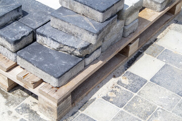 Concrete or paved gray paving slabs or floor or walkway stones stacked on a pallet. Concrete paving slabs in the backyard or road paving. Garden brick path in the courtyard on a sandy foundation.