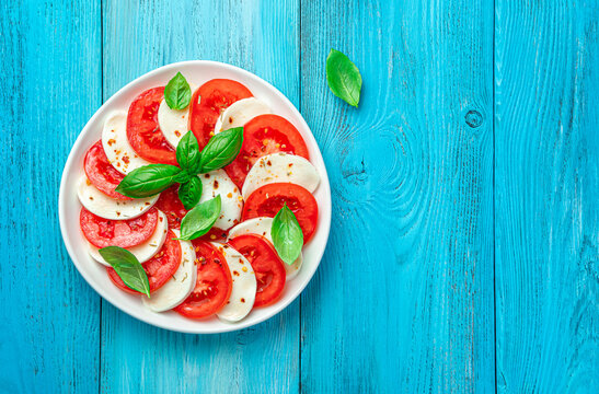Traditional caprese salad with pamidors, mazzarella, basil and olive oil on a light blue background.