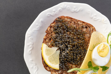 Black caviar on a sandwich with eggs, lemon, greenery